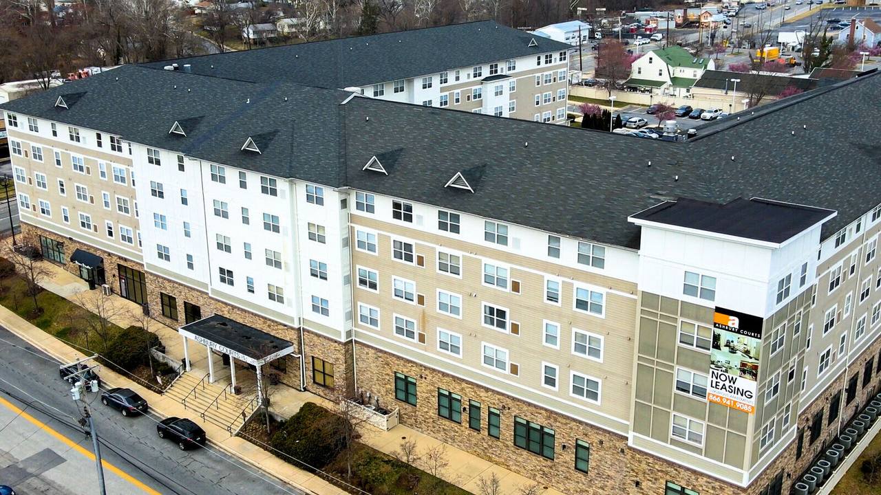 Aerial view of Ashbury Courts, a multi-story apartment building with stone-and-siding exterior and a 'Now Leasing' banner on the corner tower