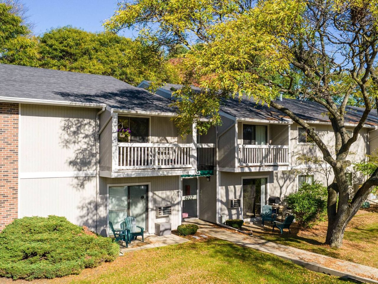 Two-story apartment building at Country Meadows with brick and wood-paneled exterior, balconies, and patio seating among mature trees